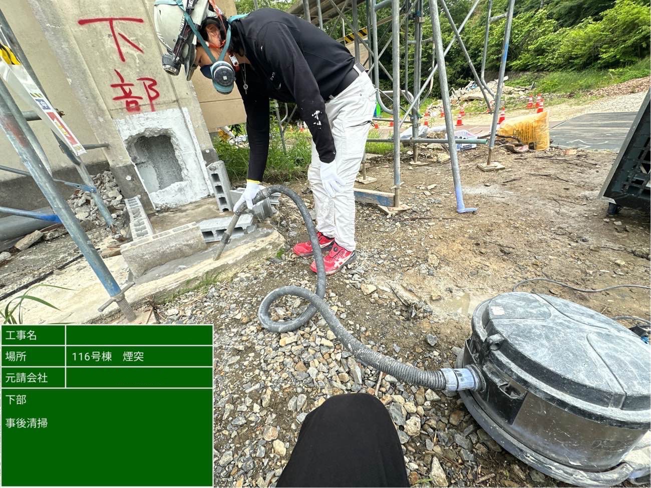 防塵マスクを着用した作業員が、煙突下部周辺を掃除機で清掃している様子