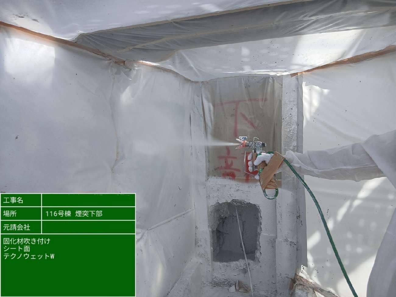 作業員が煙突下部のビニールシート面に向けて固化材をスプレーしている様子