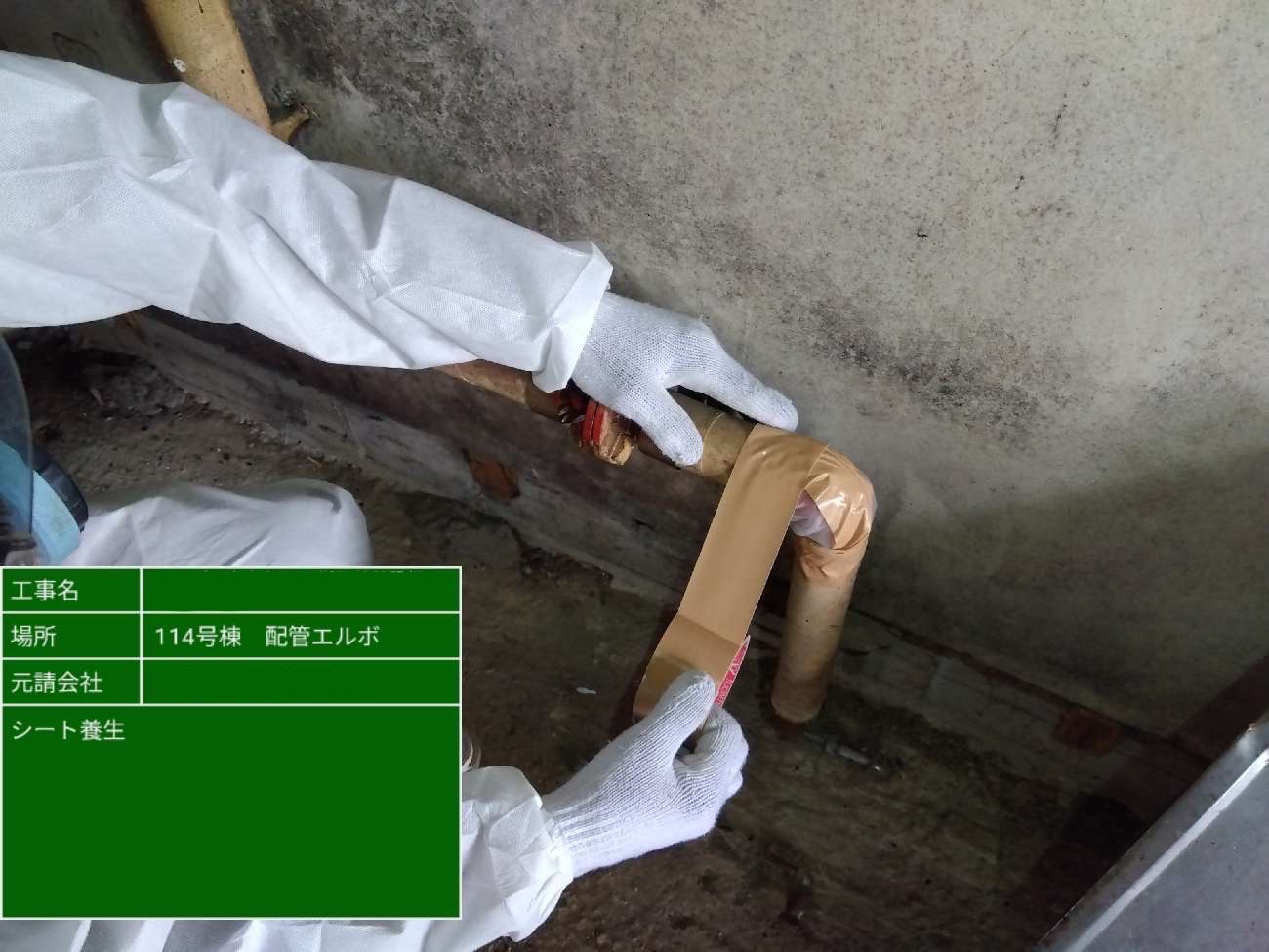 配管エルボ部分にテープを巻き、アスベスト日sン防止のためのシート養生を行う作業員の手元
